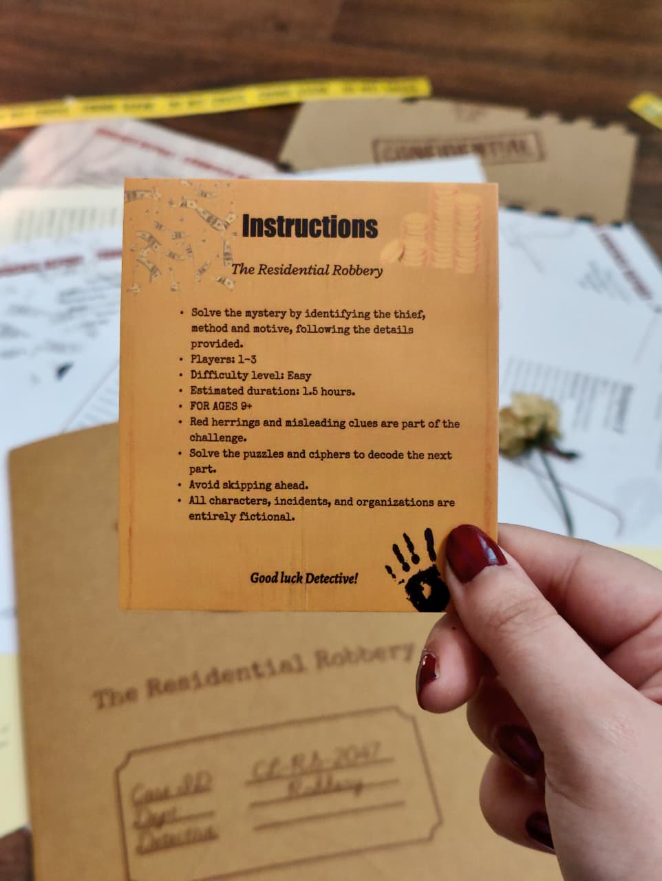 Instructions card for a mystery game held by a hand, with game materials in the background.